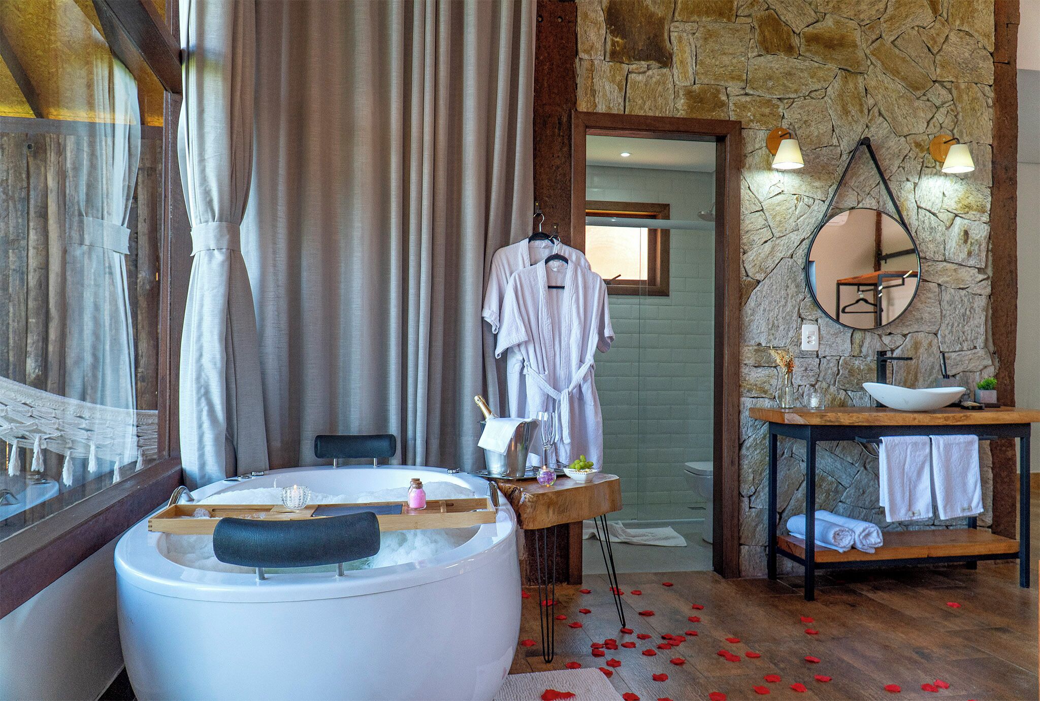 A bathroom with a stone wall, a bathtub, a mirror, and a sink with a bowl.