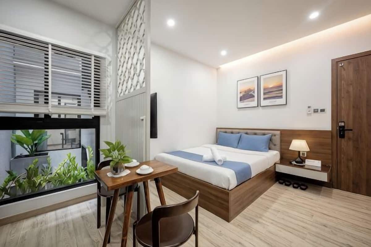 A modern bedroom with a bed, bedside table, lamp, and a view through a window.