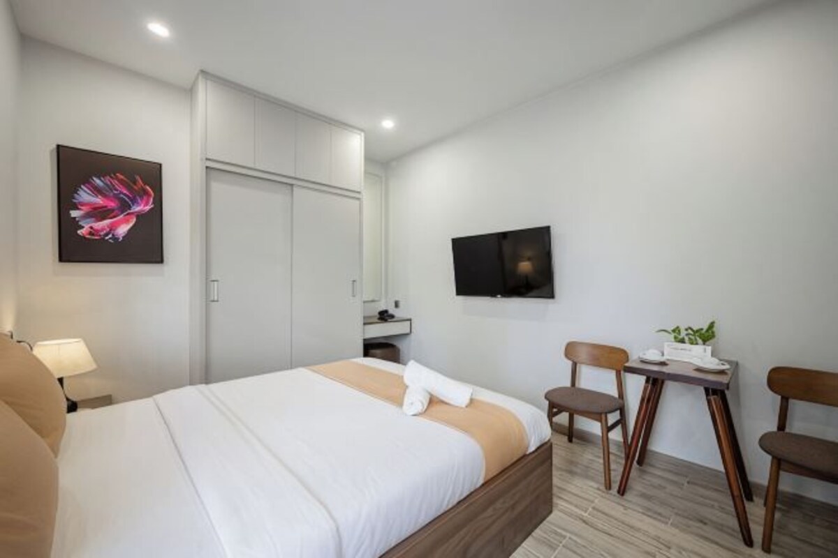 A hotel room with a bed, a desk with chairs, a TV, and a wardrobe.