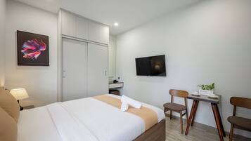 A modern hotel room with a bed, a desk, chairs, a TV, and a painting on the wall.