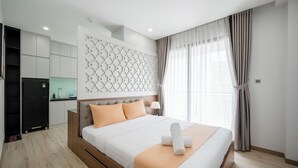 A modern hotel room with a large bed, a built-in wardrobe, a kitchenette, and a decorative wall panel.