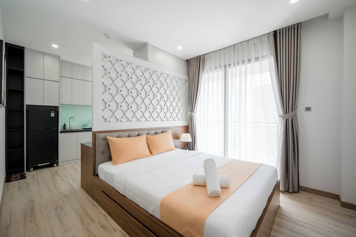 A modern hotel room with a large bed, a built-in wardrobe, a kitchenette, and a decorative wall panel.
