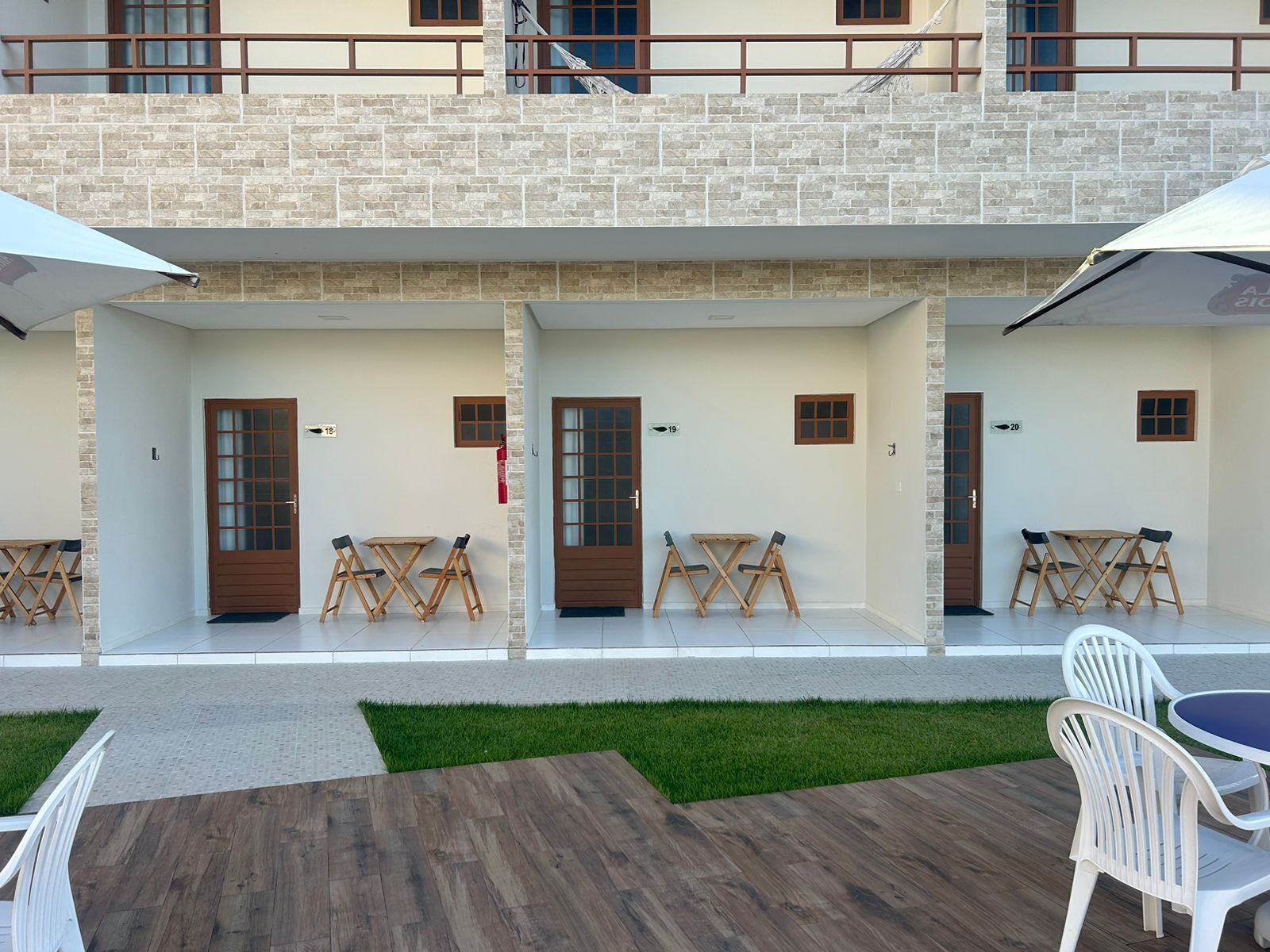 A hotel with a stone facade, multiple doors, and outdoor seating areas with tables and chairs.