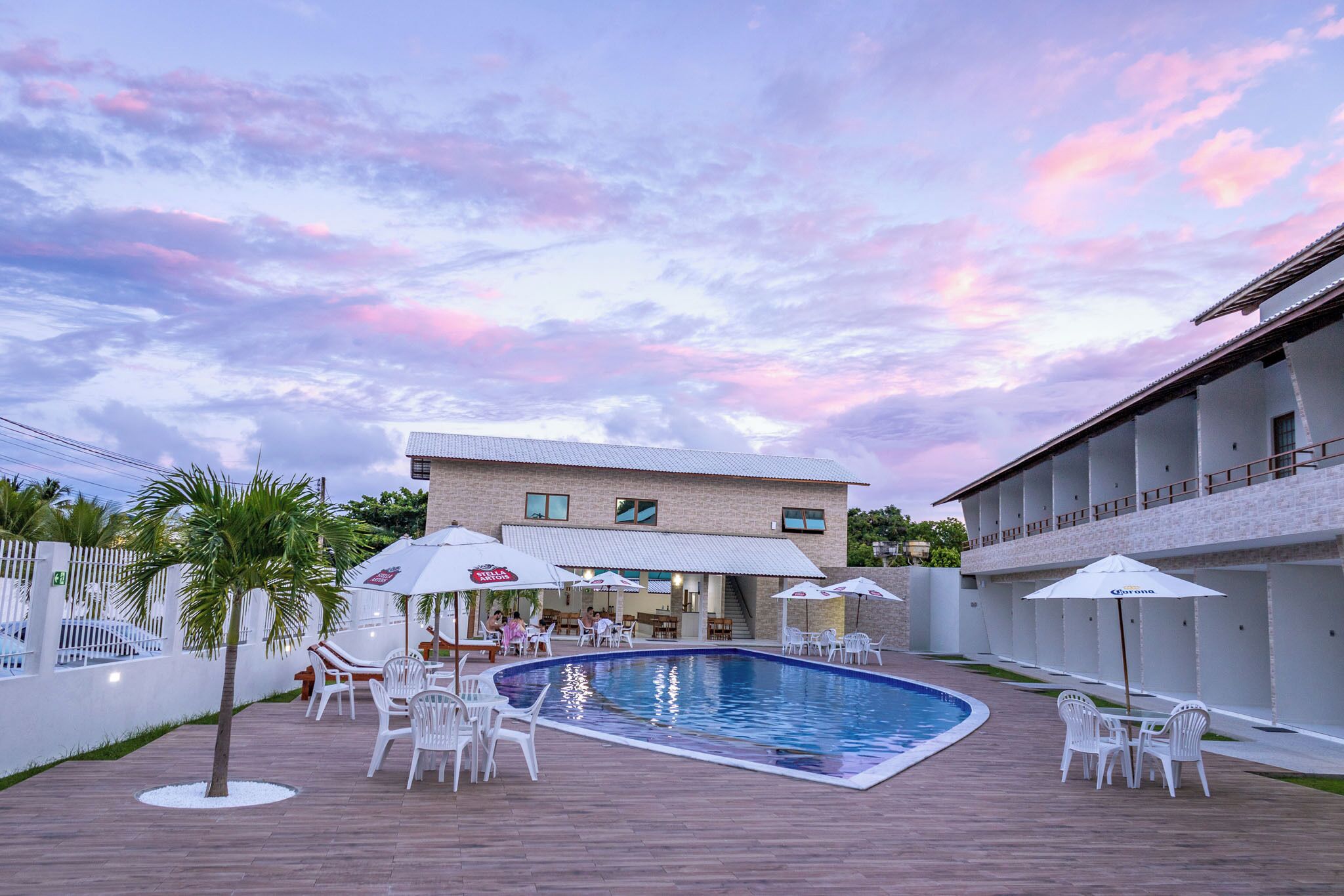 Uma área de piscina com uma piscina retangular, cadeiras brancas e guarda-sóis.