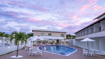 Uma área de piscina com uma piscina retangular, cadeiras brancas e guarda-sóis.