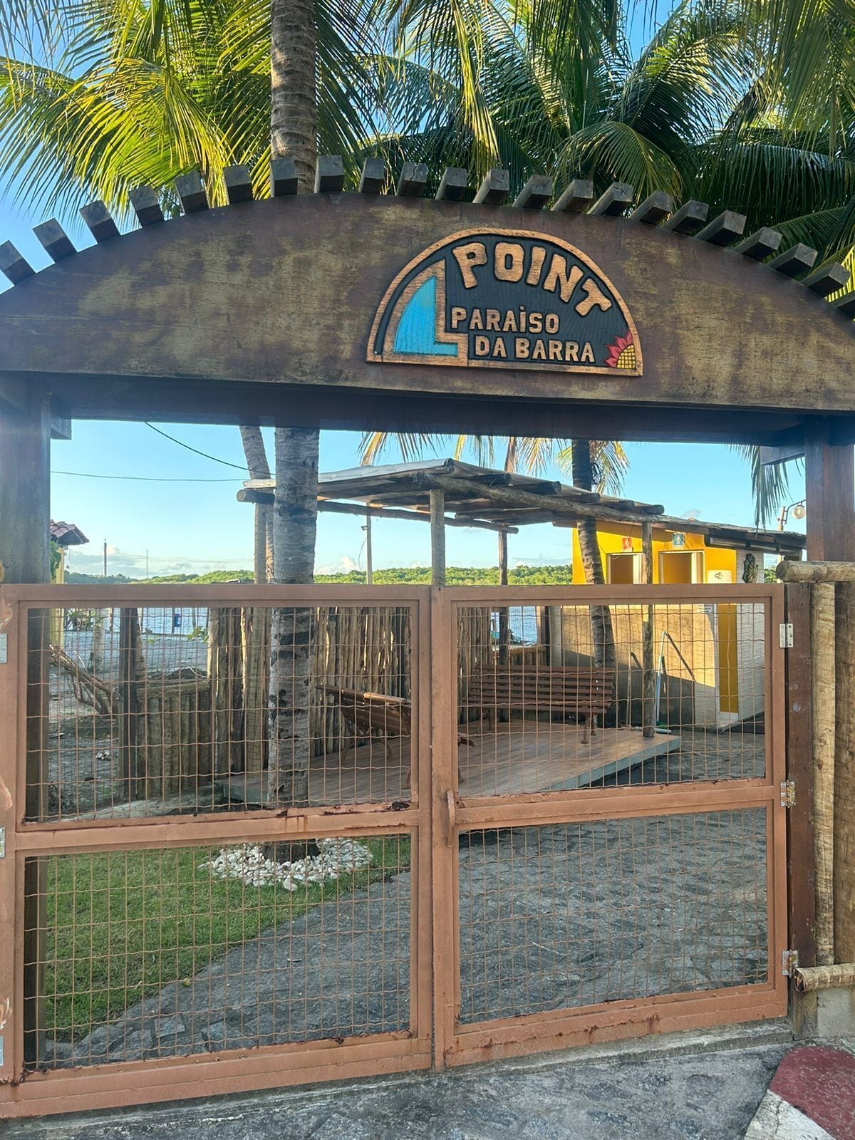 Ein hölzernes Tor mit einem Schild darüber, auf dem „POINT PARAISO DA BARRA“ steht.