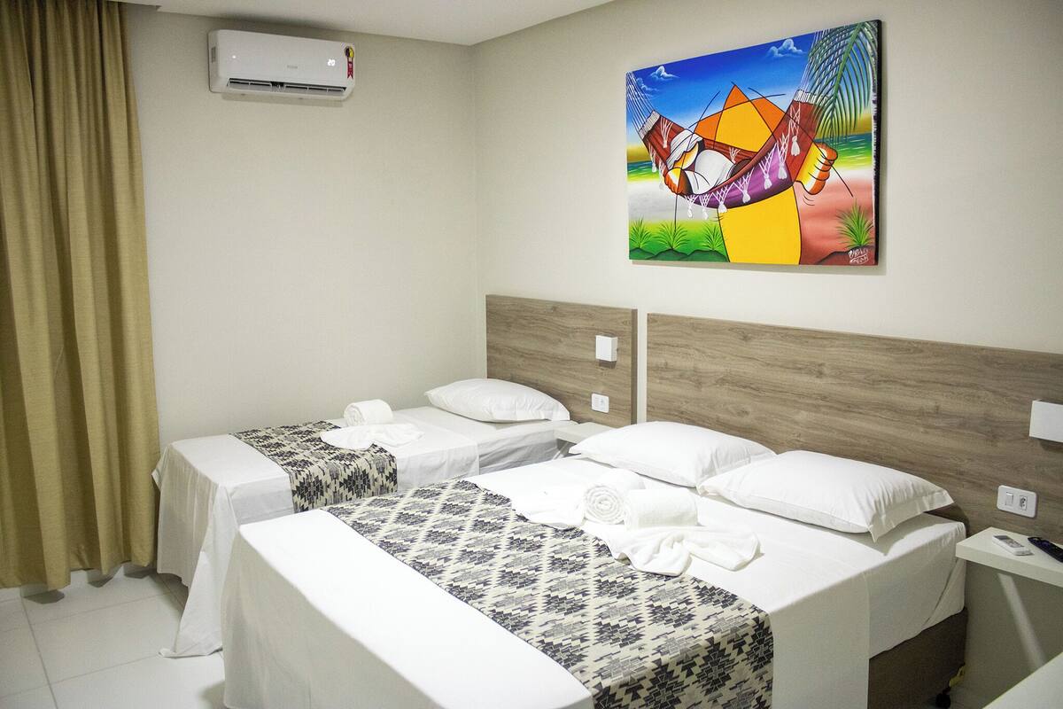 A hotel room with two beds, a wooden headboard, a painting on the wall, and an air conditioning unit.