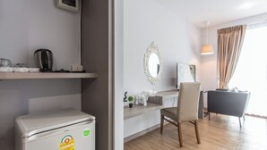 A hotel room with a compact kitchenette, a dining area with a chair and table, a large mirror, and a window with curtains. - The Earth Anthioch Khao Yai (Pak Chong)
