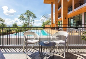 Un balcón con sillones de mimbre y una pequeña mesa, con vistas a una piscina y un paisaje montañoso.