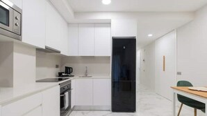 Una cocina moderna con armarios blancos, horno integrado y refrigerador negro.