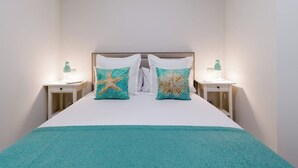 A neatly made bed with a white headboard, two matching pillows, and a teal throw blanket. There are two bedside tables with lamps on either side of the bed.