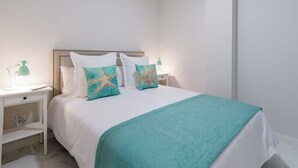 A hotel room with a bed, white walls, a teal throw blanket, and starfish-themed pillows.