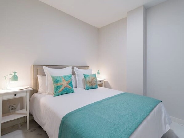 A hotel room with a bed, white walls, a teal throw blanket, and starfish-themed pillows.