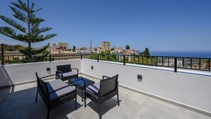 A rooftop terrace with outdoor furniture, a view of the sea, and buildings in the background.