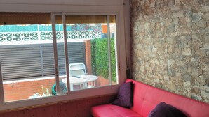Een kamer met een rode bank, een stenen muur, een plafondventilator en een raam met uitzicht op een tuin en een gebouw.