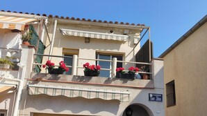 Een gebouw met twee verdiepingen, een balkon versierd met rode bloemen, een zichtbaar straatnaambord en een gesloten luik.