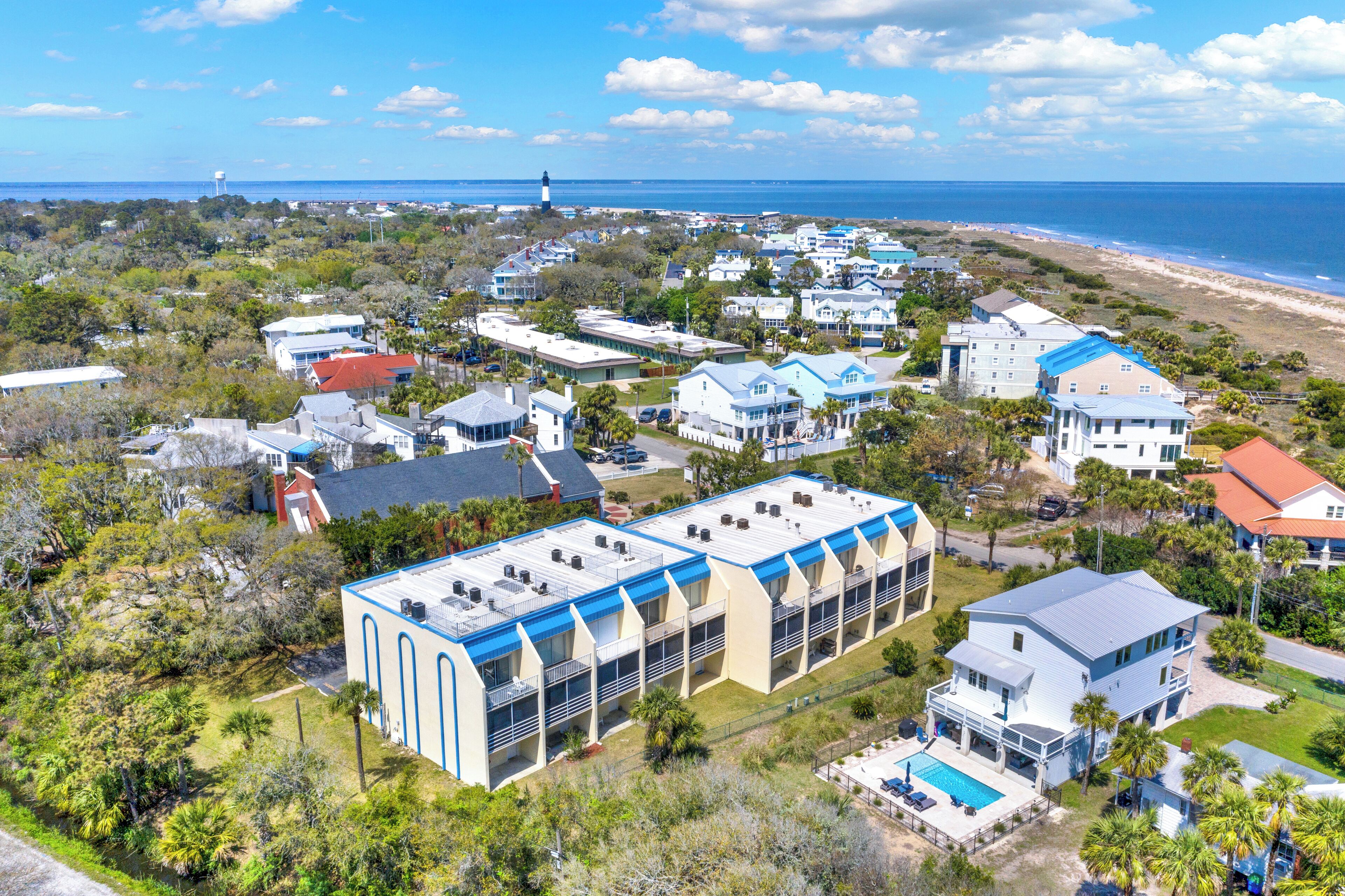 Zona residencial costeira com casas, piscina e um farol ao fundo.