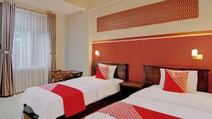 A hotel room with two beds, a wooden nightstand, a chair, and a window with curtains.
