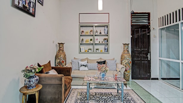 A living room with a brown sofa, a glass coffee table, a patterned rug, and decorative vases.