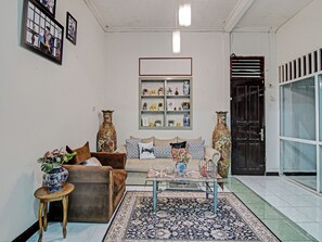 Un salon avec un canapé marron, une table basse en verre, un tapis à motifs et des vases décoratifs.