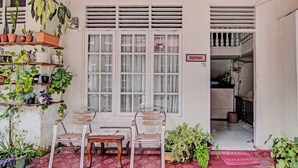 A covered outdoor seating area with a table and chairs, surrounded by potted plants and a 'RESEPSIONIS' sign.