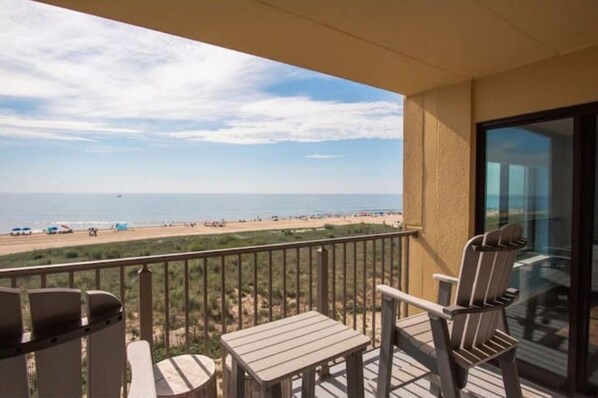 A balcony with a view of the beach, featuring two Adirondack chairs and a small table. - Oceanfront Condo w/ Direct Beach Access (Ocean City)