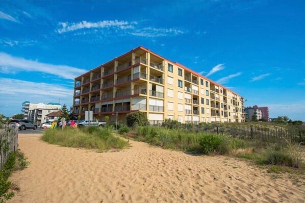 A multi-story hotel with a flat roof, located near a sandy beach.
