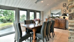 A dining area with a large table, chairs, and a vase of flowers. There is a stone wall and a wooden cabinet in the background. - Chez Marie-Céline - Maison avec jacuzzi à 20 min du Val André (Plestan)