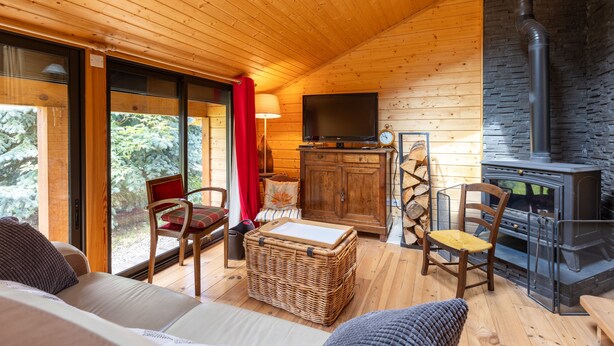 A cozy cabin interior with a wooden ceiling, a stone fireplace, a television, and a comfortable seating area with a sofa and chairs.