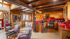 A spacious kitchen with wooden cabinets, a red backsplash, and a central island. There are wooden chairs and a dining table with chairs.