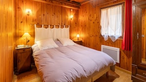A wooden-paneled room with a bed, two bedside lamps, a radiator, and a wardrobe.