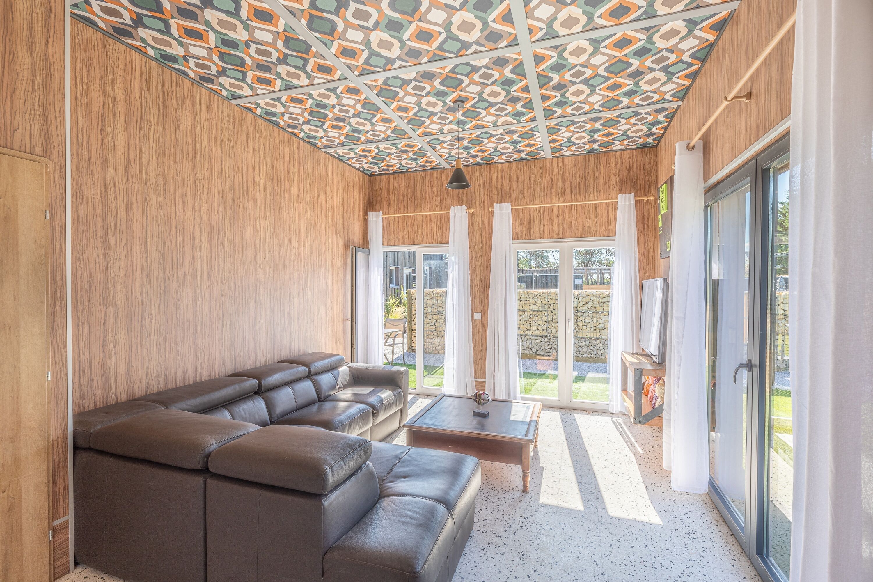 A modern living room with a sectional sofa, a coffee table, and a patterned ceiling.