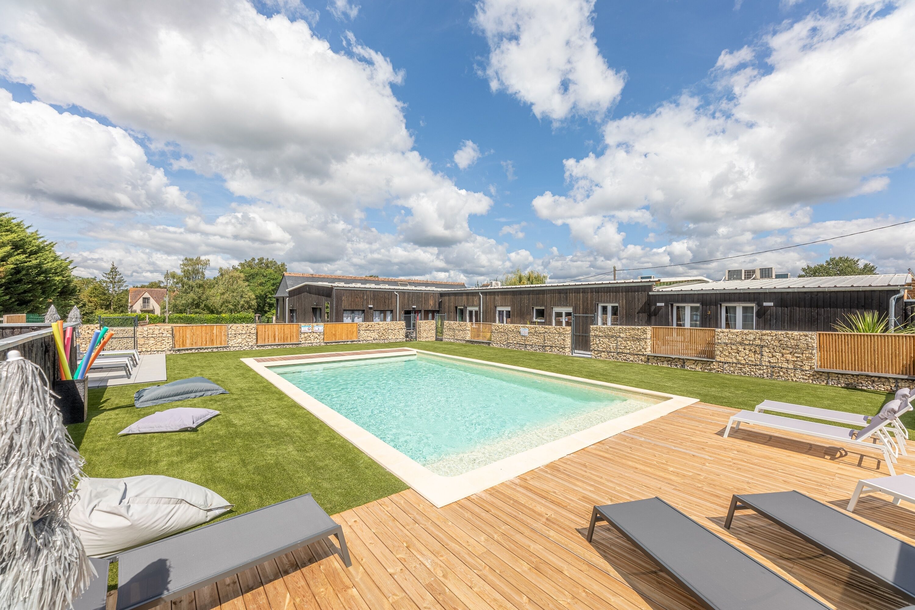 Un espace piscine doté d’une terrasse en bois, de chaises longues et d’un mur en pierre.