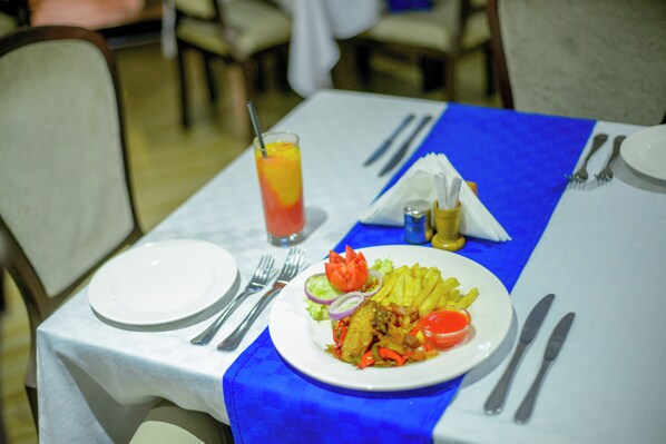 A dining table with a blue table runner, a plate of food, cutlery, and a glass of orange juice.