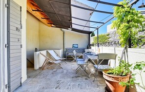 Relax on the patio with a table, chairs, and a bench, surrounded by a metal roof and a potted plant.