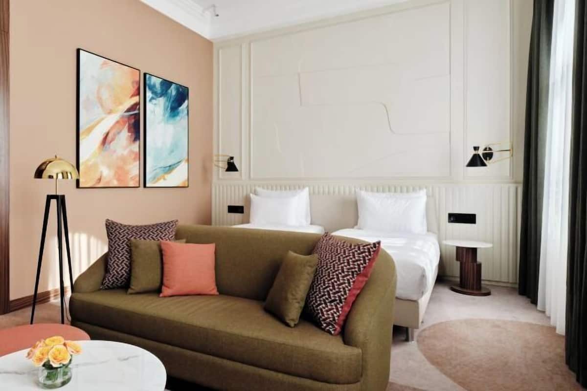A hotel room with a sofa, a bed, a round coffee table, and two wall-mounted lamps.