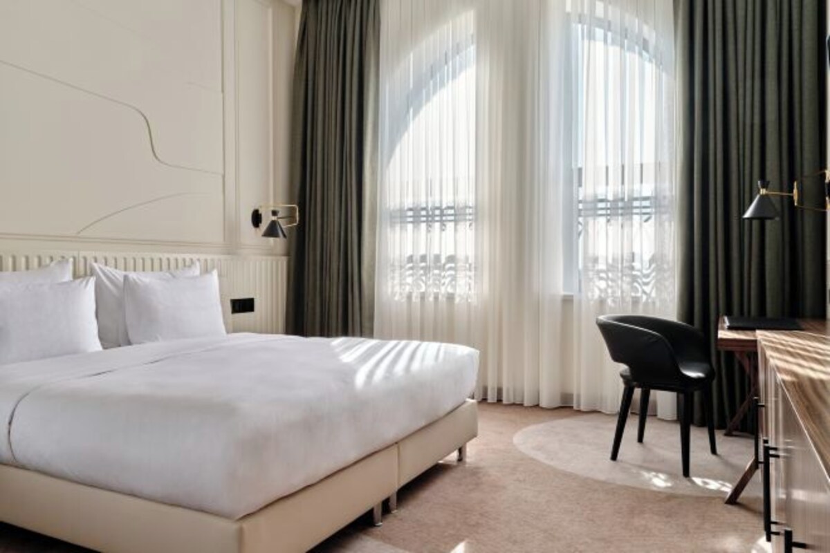 A modern hotel room with a large bed, a desk, and a chair.