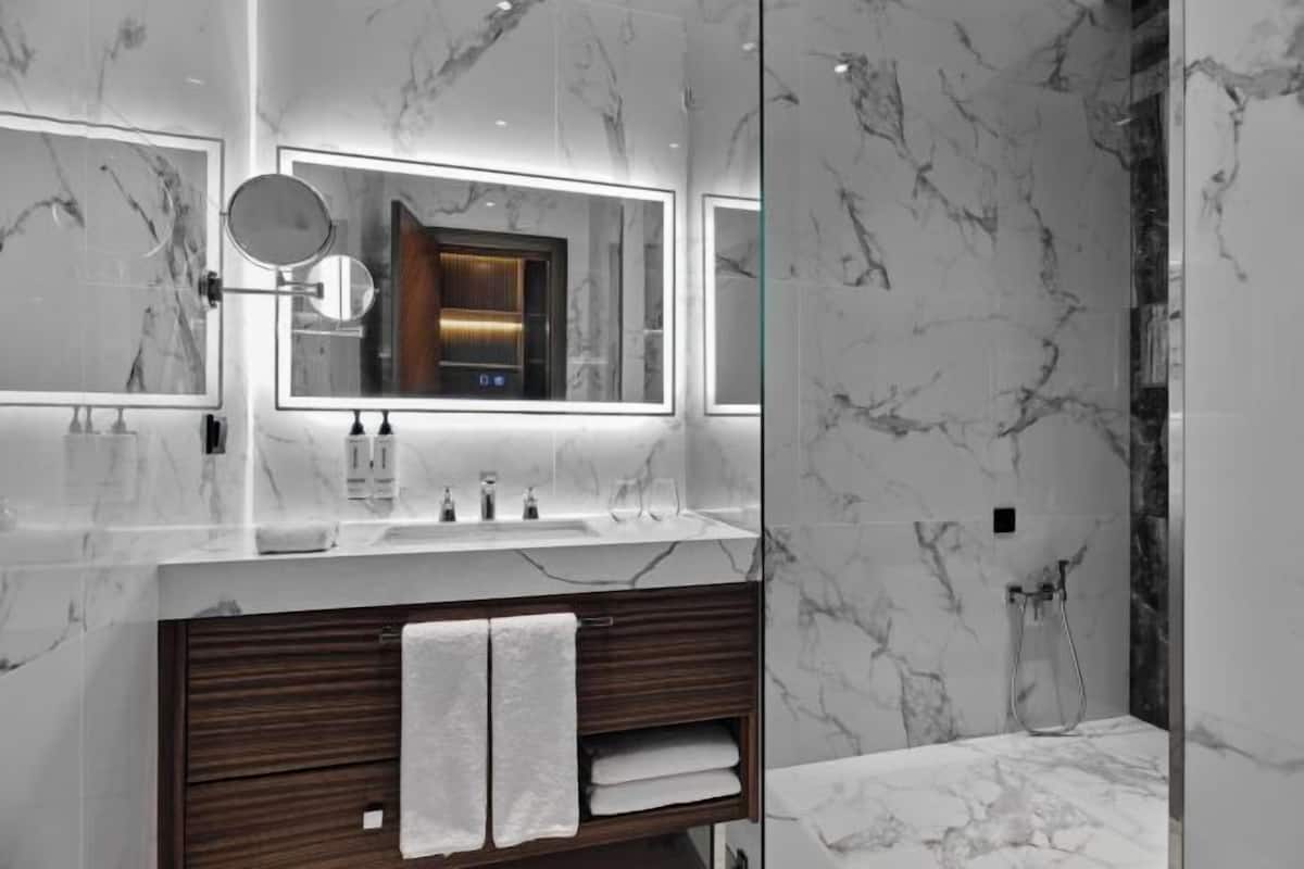 A modern bathroom with marble walls, a wooden vanity, two sinks, and a large mirror.