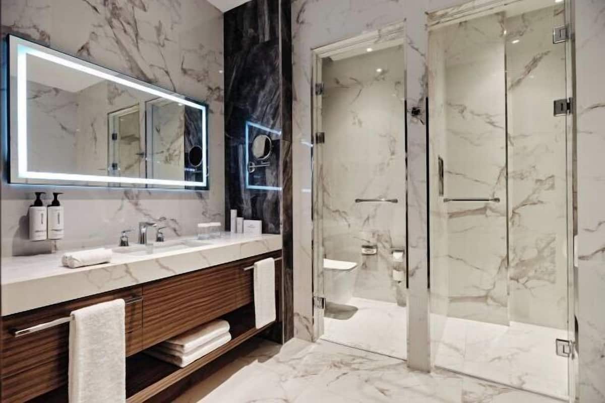 A modern bathroom with a marble vanity, a large mirror, and a glass-enclosed shower.