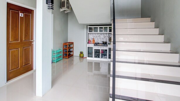 A hallway with a wooden door marked with the number 3, a staircase with white steps, and a kitchen area with cabinets and a gas stove. - OYO 92477 Anugrah Kostel Syariah (Semarang)