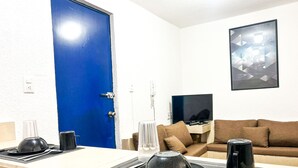 Un coin repas avec une table dressée pour deux personnes, une porte bleue, un canapé marron et une œuvre d’art abstraite encadrée accrochée au mur.