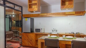 Une cuisine compacte équipée d’un réfrigérateur, d’un four à micro-ondes et d’un évier. On y trouve deux chaises et une table avec un set de table vert.