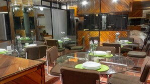 Un espace repas moderne avec des tables en verre et des chaises en osier, équipé d’assiettes, de tasses et de couverts.