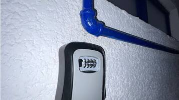 A white textured wall with a blue pipe and a small, rectangular device with a black and white label.
