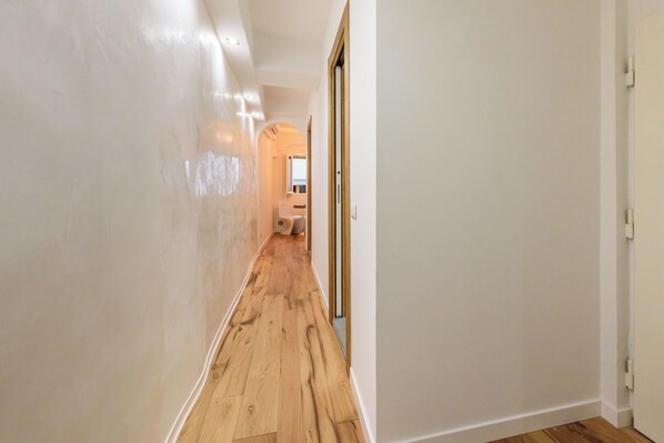 A hallway with wooden flooring and white walls, leading to a room with a window and a door. - Casa Maria by Mmega (Florence)