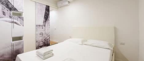 Et hotelværelse med seng, hvide sengetøj, sengegavl, et klædeskab og en vægmonteret aircondition.