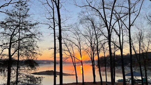 A lakeside deck with benches and a railing, overlooking a sunset over the water. - House on Smith Lake! No steps to water/dock! 4 bedrooms & 3 full baths. (Jasper)