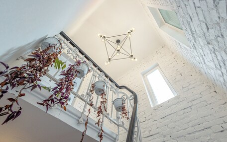 A staircase with a white brick wall, a hanging plant, and a geometric ceiling light fixture.