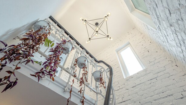 Een trap met een witte bakstenen muur, een hangende plant en een geometrisch plafondarmatuur.