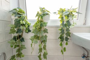 A bathroom with three potted plants hanging from the window, a white sink, and a tiled wall. - First Hostel Bucur 21 (Bucharest)